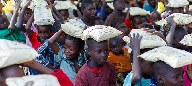 A group of underprivileged children carry bags of VitaMeal on their heads.
