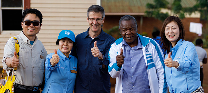 Nu Skin Founder Steve Lund, Napoleon Dzombe, and Nu Skin sales leaders and employees pose for a picture by giving a thumbs up.