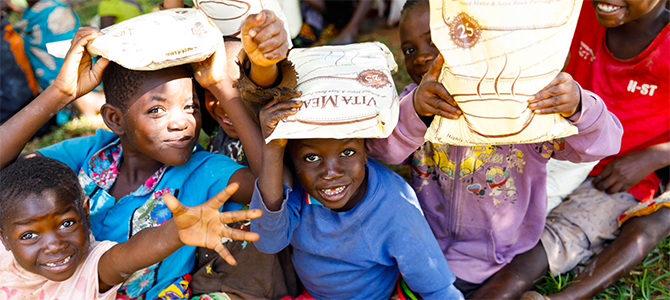 Children from the Mtendere Orphanage pose for a picture with their bags of Vitameal given to them from the Nourish The Children Initiative.