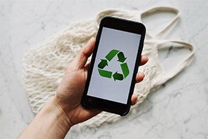 person holding a smartphone with recycle logo on the screen