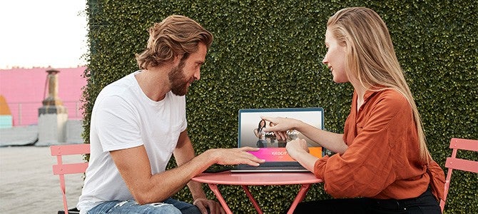 two people sitting at a table looking at a laptop