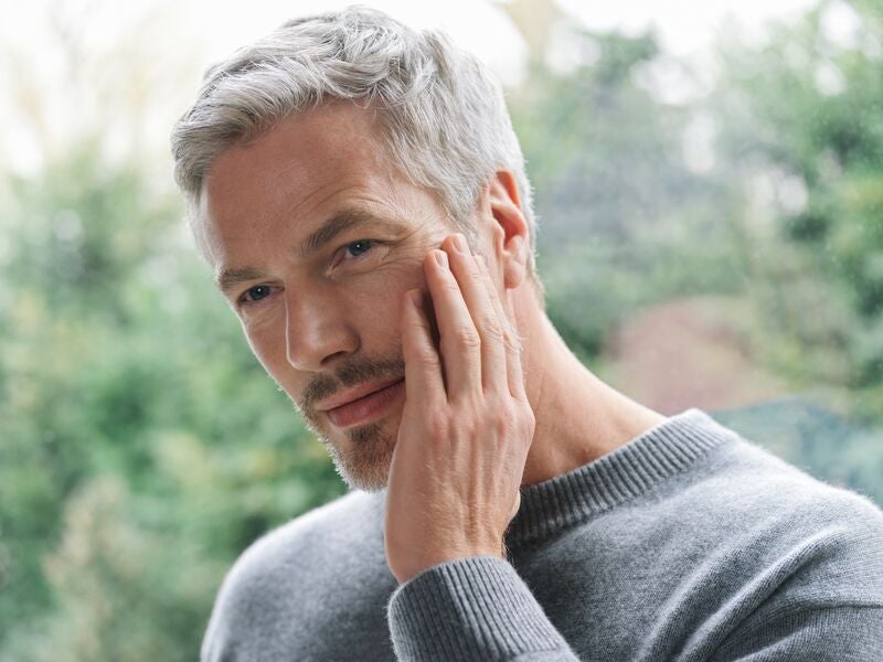 Middle-aged male with gray hair holding hand up to feel his recently moisturized face