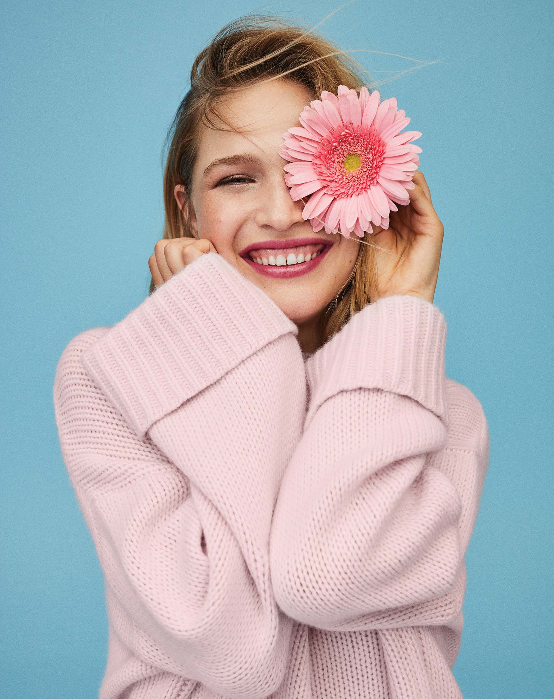 Youthful woman smiling and holding a flower over one eye