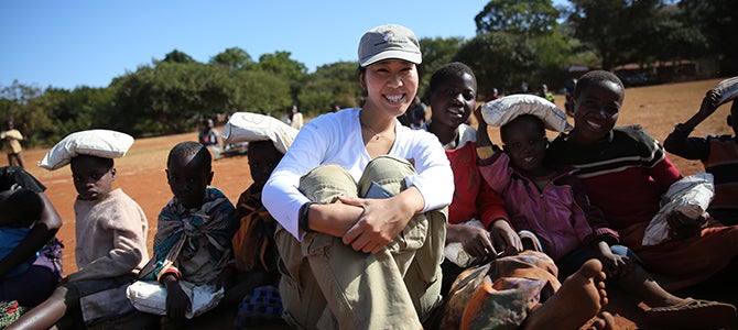 A Nu Skin sales leader sits with Malawi children as they receive bags of VitaMeal.